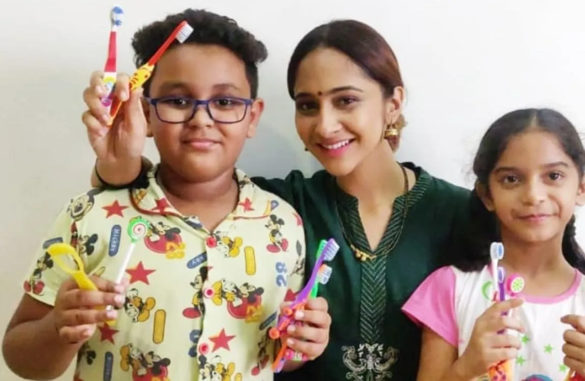 A mother and two children holding MAXI kids toothbrushes and tongue cleaners